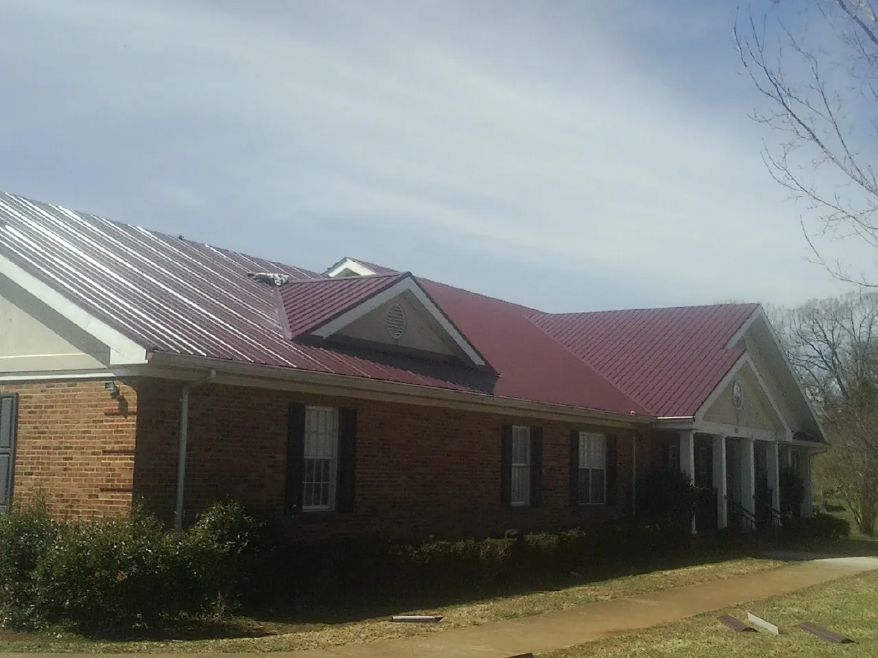 Red metal roof with gabled entries on a long brick building, from a Hail Damage Roof Repair job in Cardington