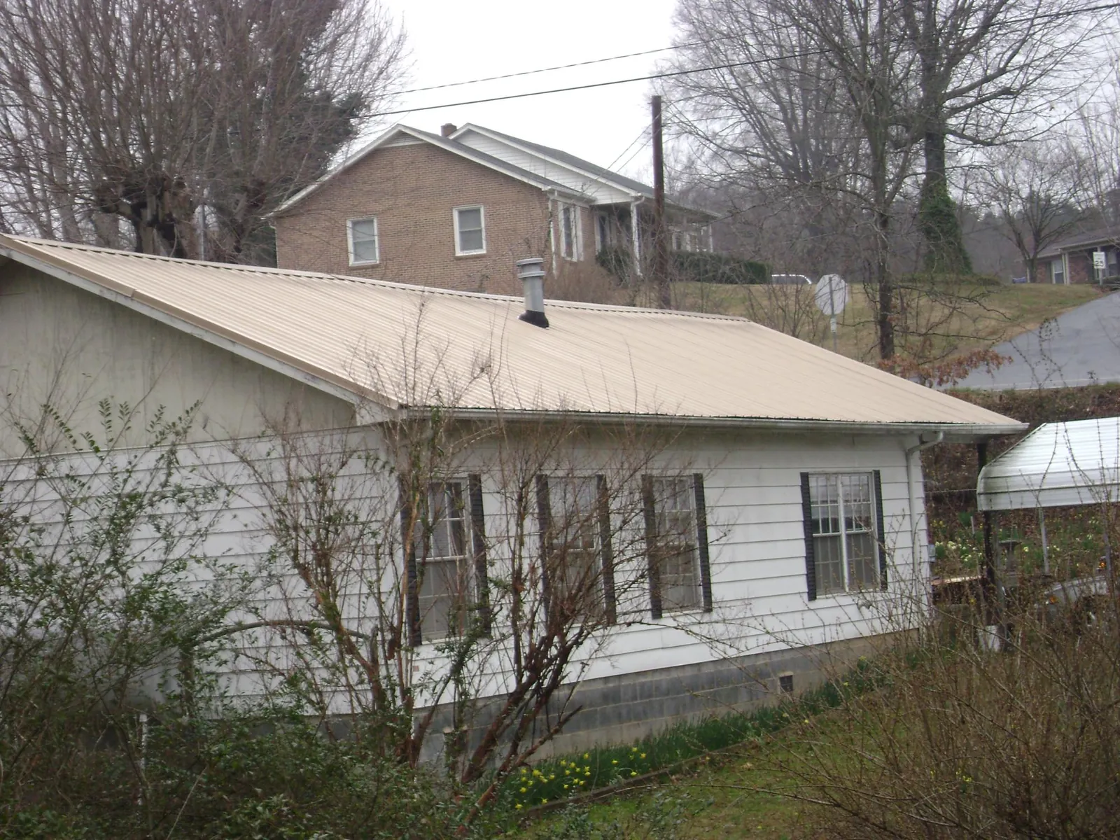 Tan metal roof on a white sided house set into a hillside — Commercial Roofing by Roofing Brothers in Cardington