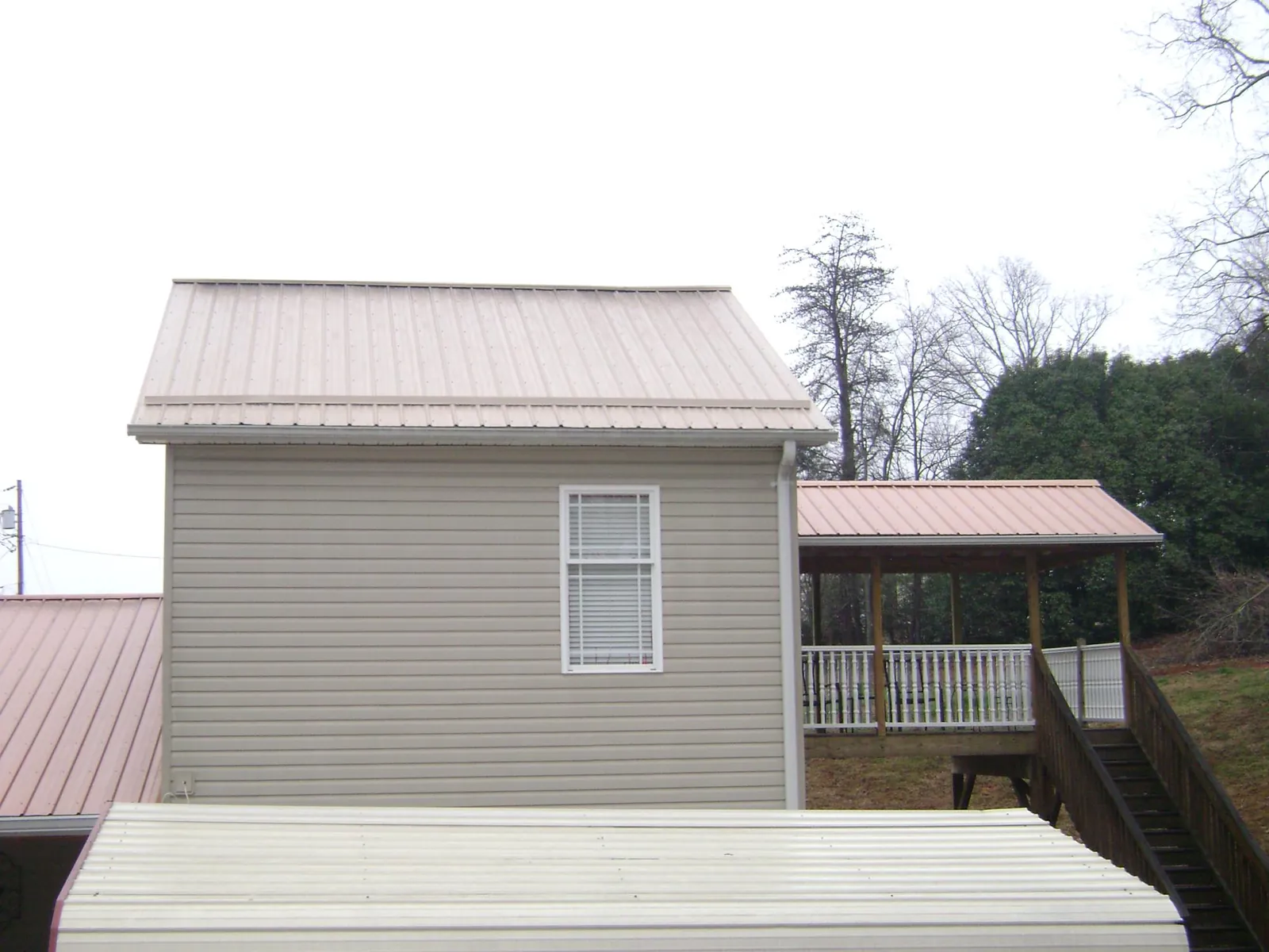 Tan metal roofs on a two story addition and attached porch, from a Roof Replacement job in Cardington